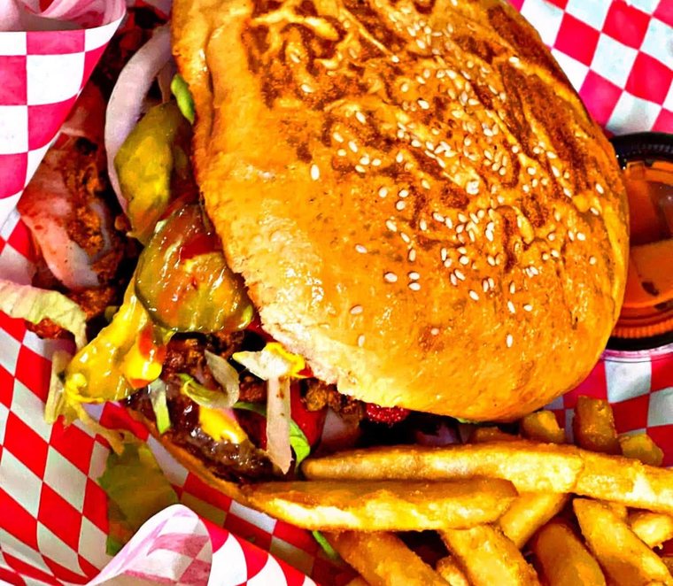 The Pumbah Burger on a seeded bun with fries, in a red basket. Photograph posted by Pumbah's Tacos & Burgers.