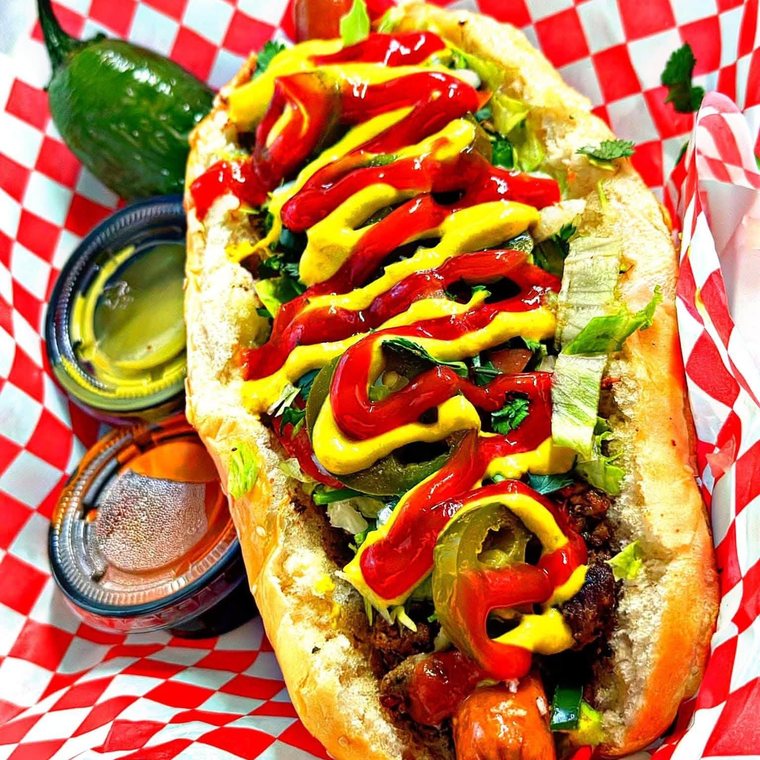 The Pumbah Hotdog under mustard and ketchup with jalapenos, in a red basket. Photograph posted by Pumbah's Tacos & Burgers.