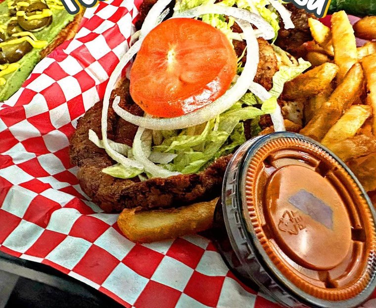 Torta de milanesa with tomato, onion and lettuce, in a red basket with fries. Photograph posted by Pumbah's Tacos & Burgers.